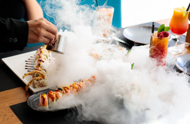 liquid smoke being poured onto plates of sushi on a table