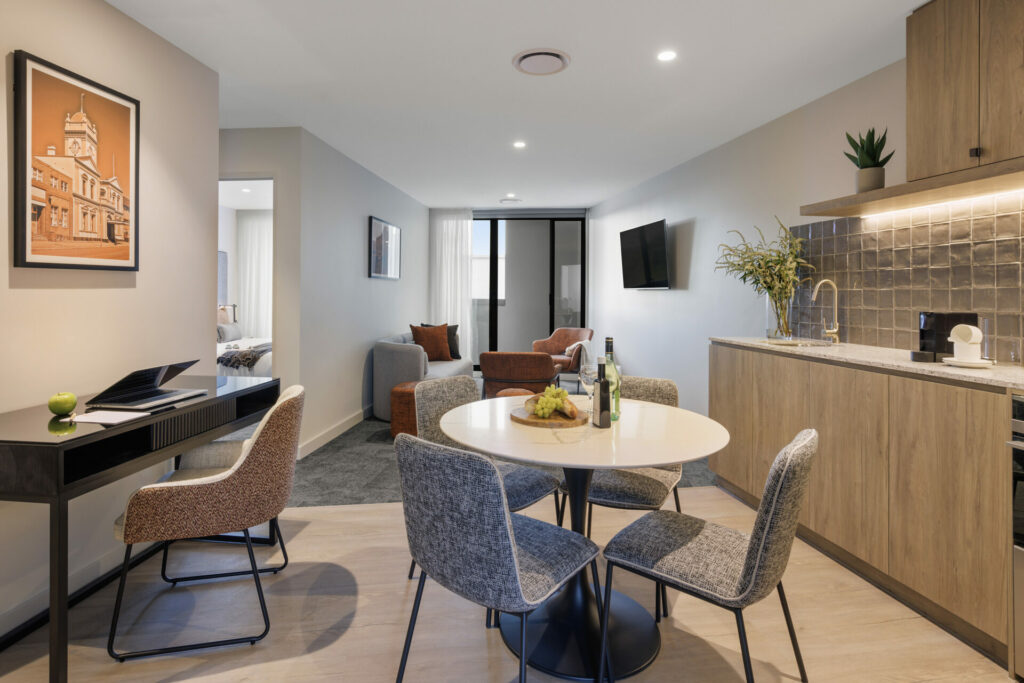 Living room angle 2 Living area, sofa, coffee table, study desk, chairs, TV, dining table and chairs, outdoor balcony access, 2 bedroom apartment hotel